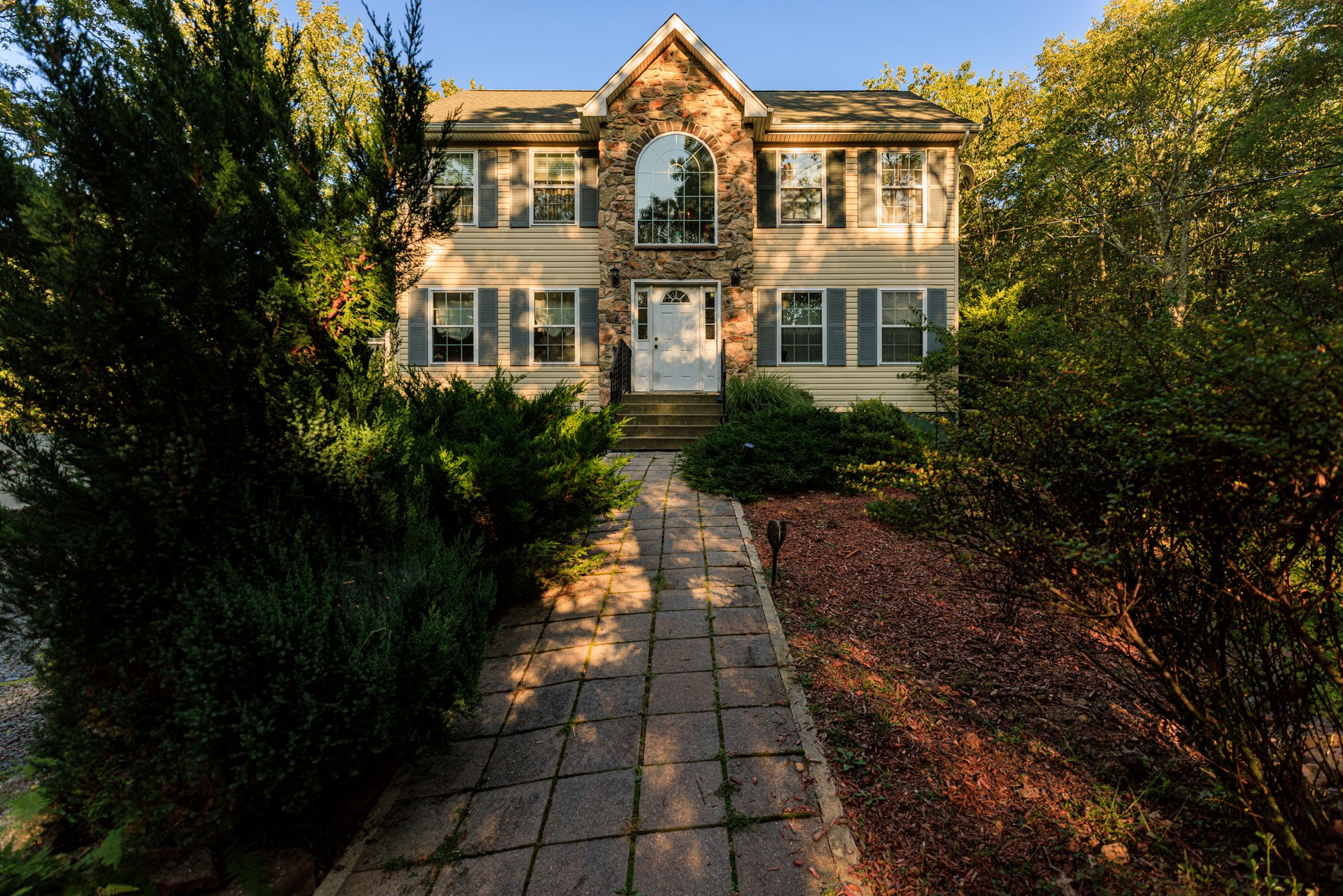 Nestled in Poconos forest. Two-story middle-class home with stone facade and beige siding